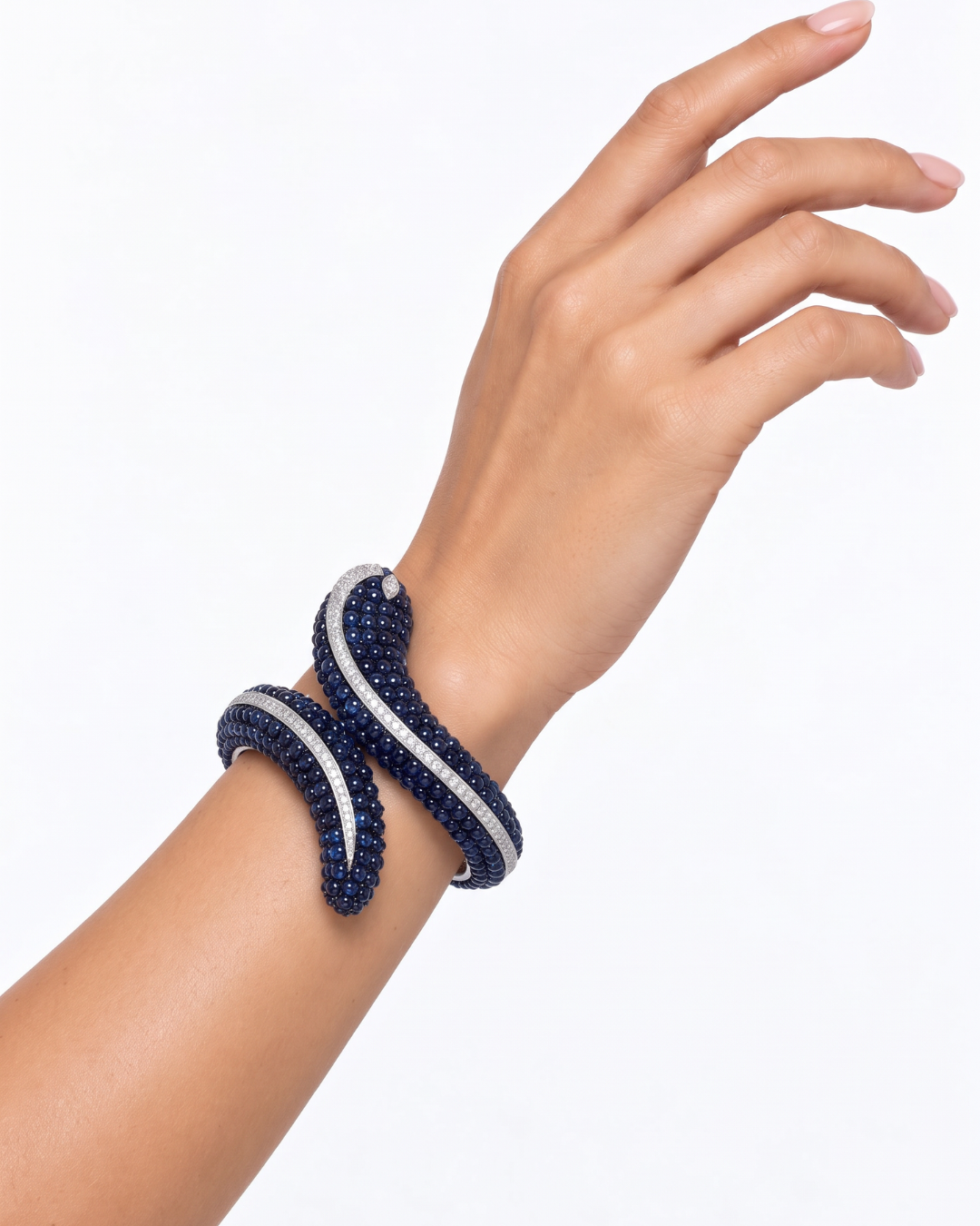 A close-up of a person's wrist and hand wearing a coiled bracelet made of dark blue and silver-toned pavé-set stones, photographed against a clean white background.