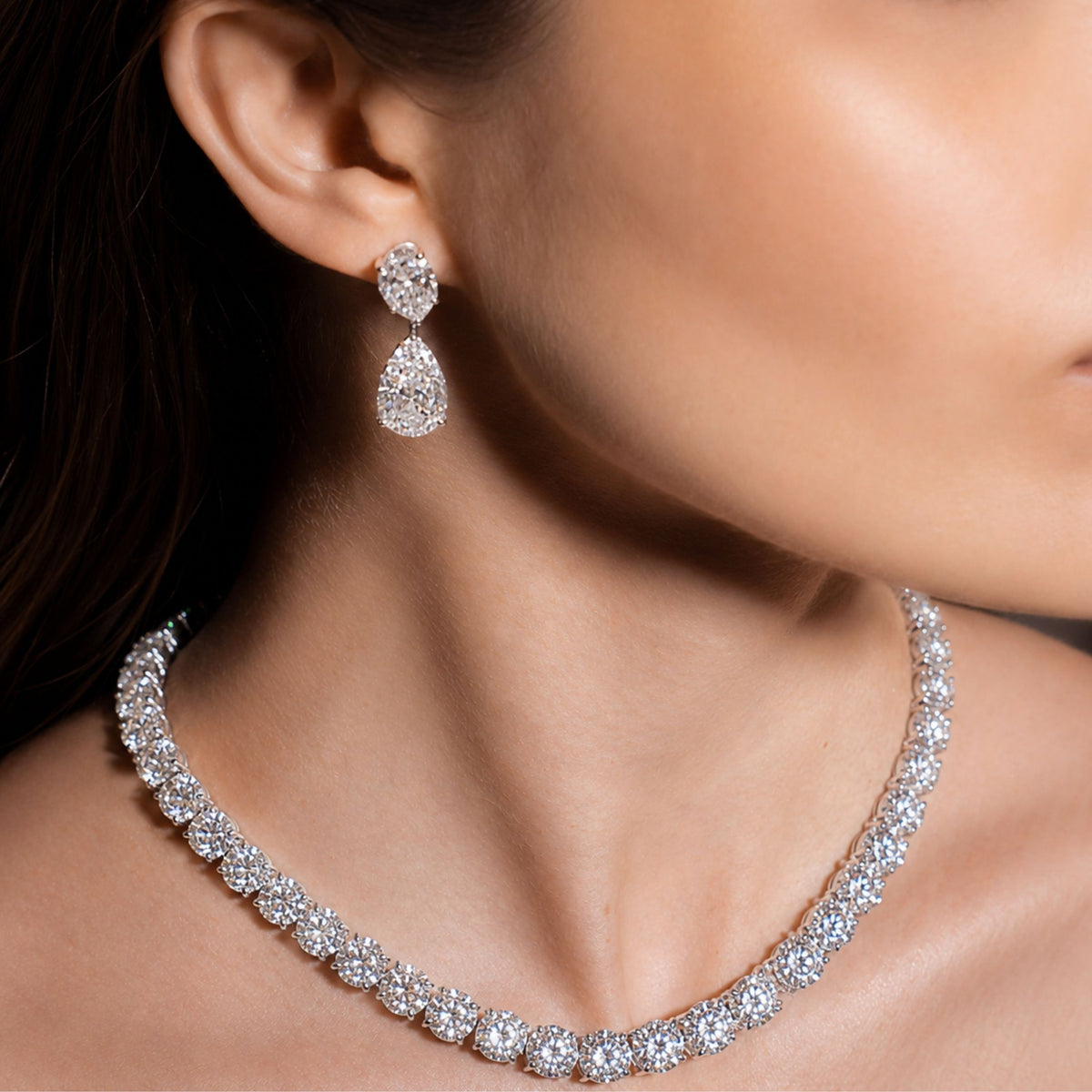 Woman wearing platinum diamond rivière necklace with graduated silhouette and matching two-tier drop earrings