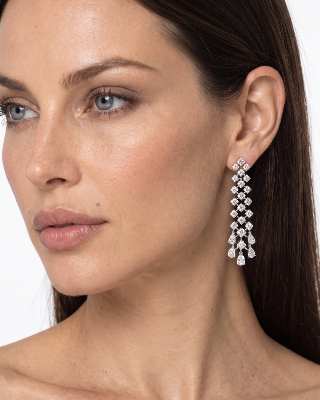 A close-up of a woman wearing a long, multi-tiered drop earring made of diamonds in a 18K white gold setting.