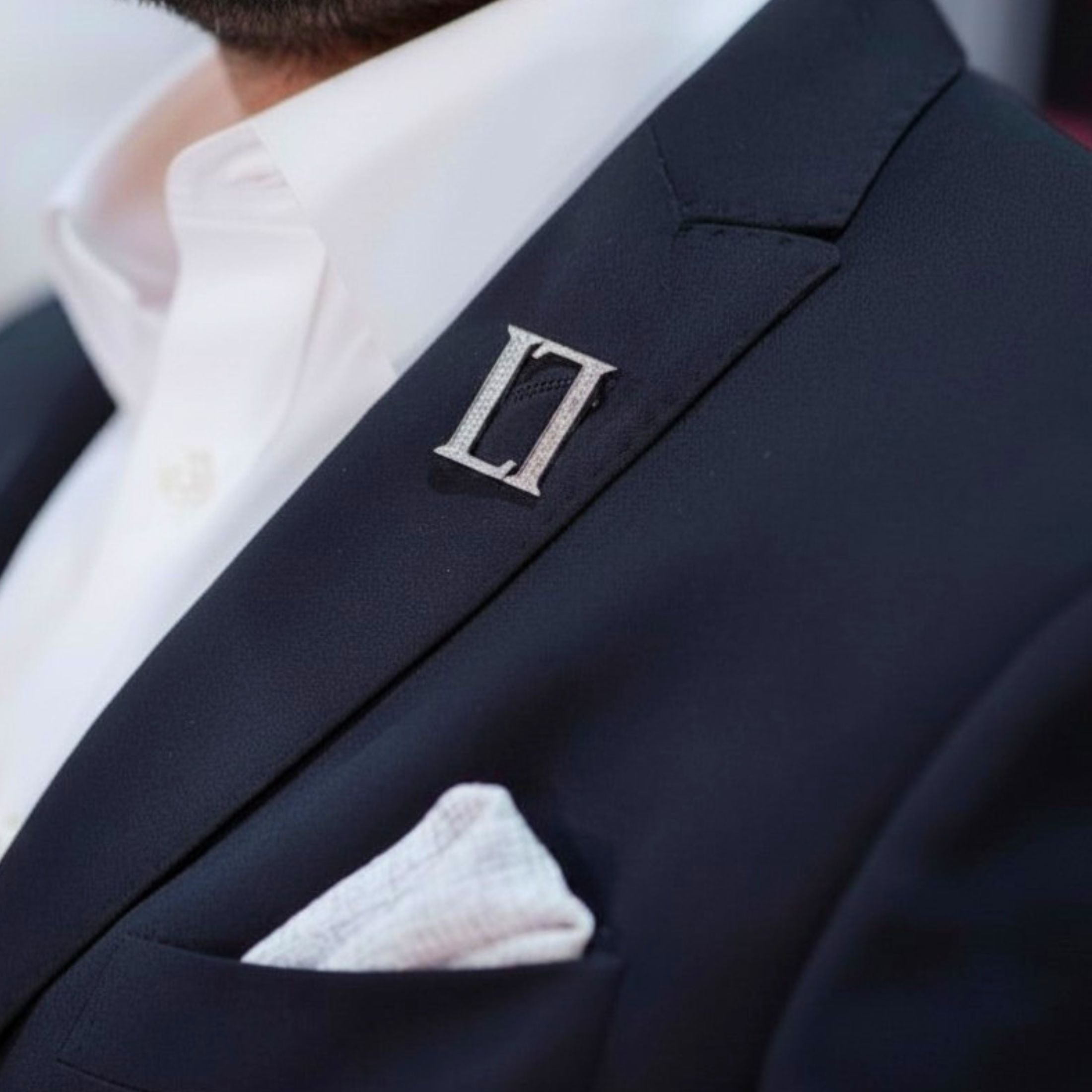 Leviev platinum diamond lapel pin letter L on navy suit