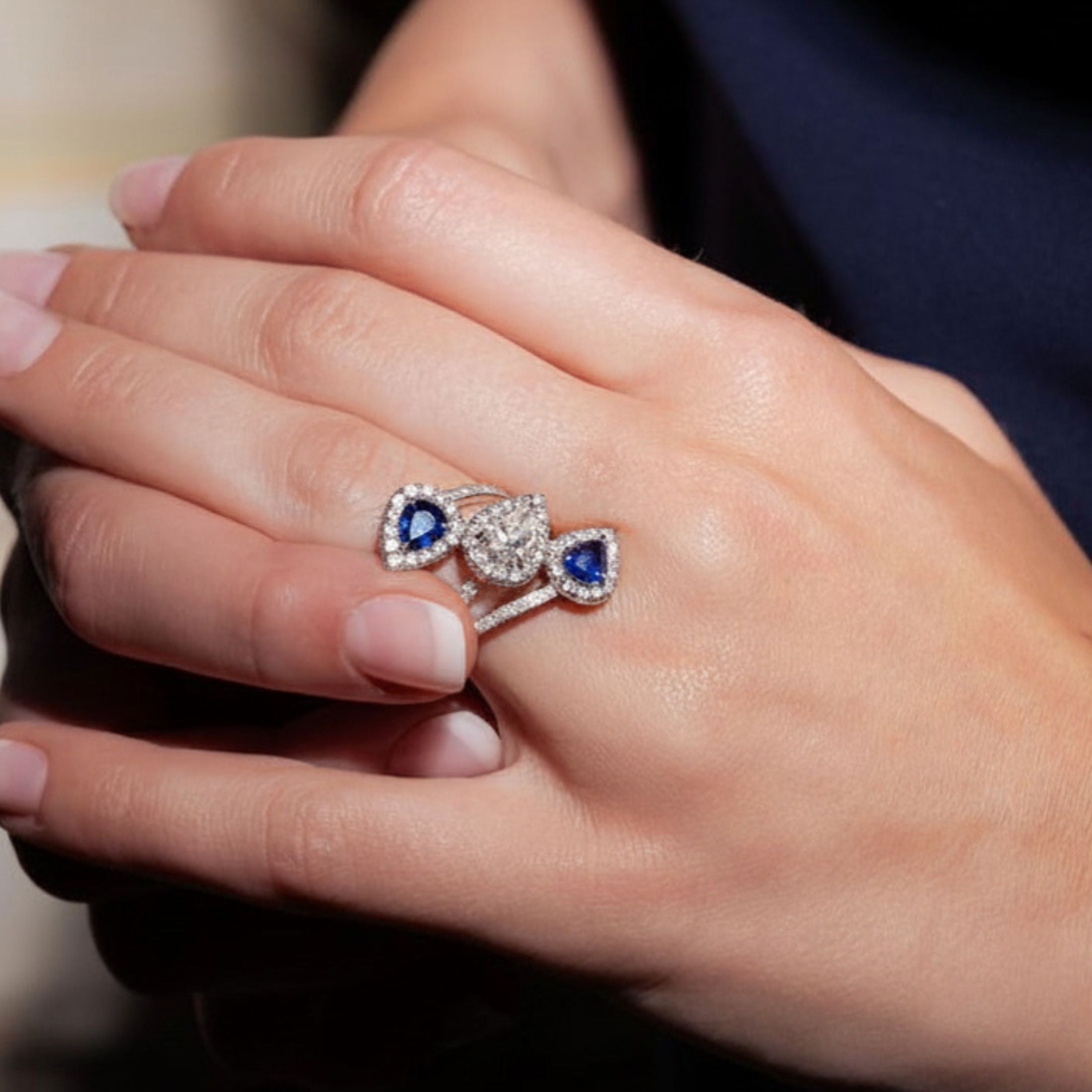 Woman wearing Leviev Reko bypass ring on left hand featuring royal blue sapphire and pear diamond design in 18K white gold