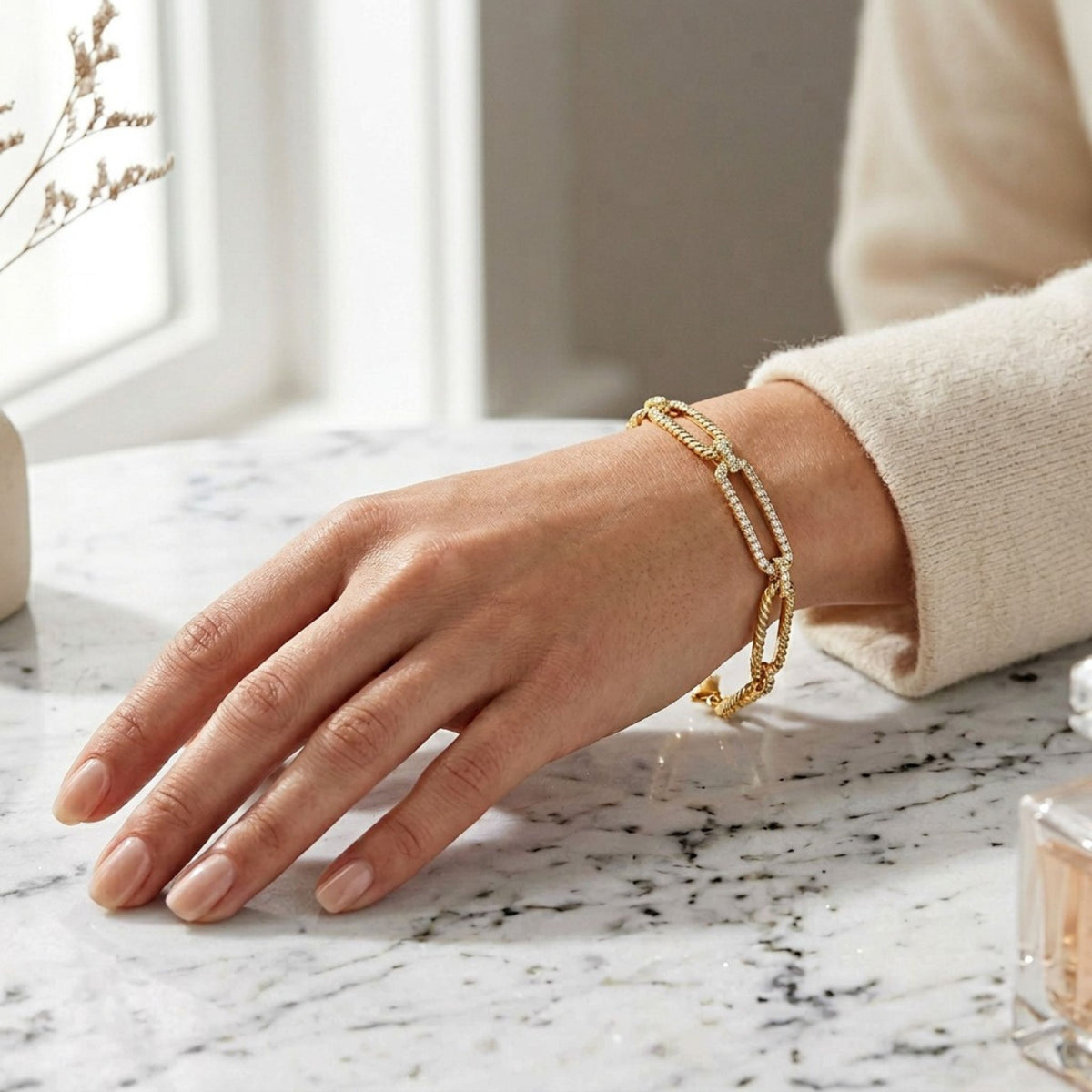 Woman wearing 14K yellow gold twisted link diamond bracelet on wrist with cream sweater sleeve