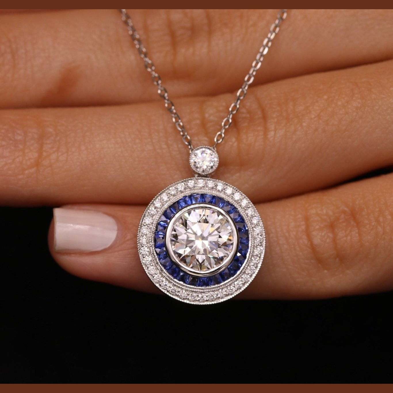 Close-up of Leviev bezel-set round diamond pendant surrounded by deep royal blue sapphires and diamond halo in 18K white gold